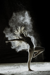 Obraz na płótnie Canvas Rebirth - Young dancer traces patterns through a cloud of powder as she dances against a dark background