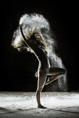 Fototapeta na wymiar Joy - Young dancer traces patterns through a cloud of powder as she dances against a dark background