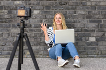 Cute blond female blogger with laptop recording video