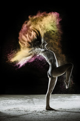 Fototapeta na wymiar Power Kick - Young dancer traces patterns through a cloud of powder as she dances against a dark background