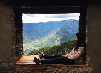 A female traveler sitting inside a window in the wall on the top of a mountain in Paro, Bhutan