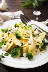 Plate of ravioli with broccoli, goat cheese and herbs on old wooden background. Italian healthy food concept.