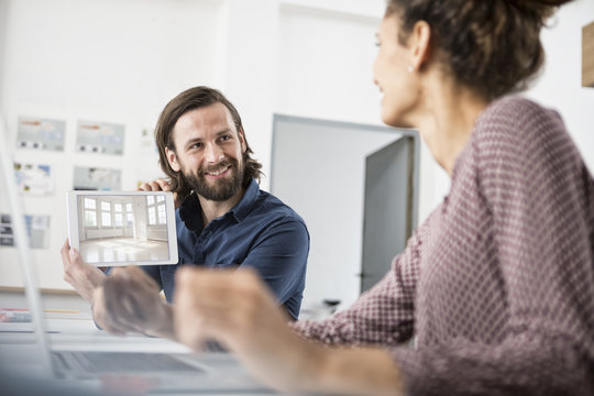 Smiling man showing colleague picture of an apartment in office
