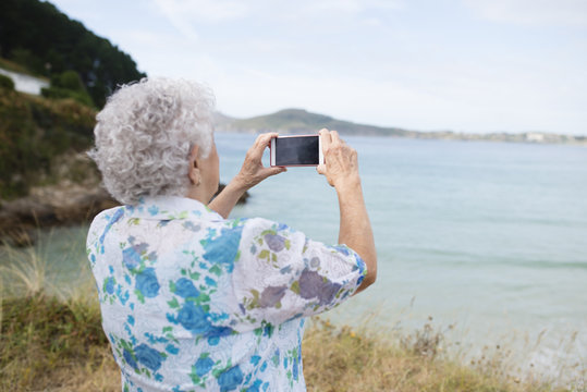 Back view of senior woman taking picture from the sea with smartphone