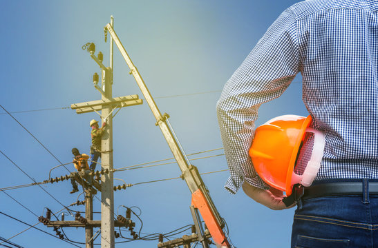 electrical engineer holding safety helmet with electricians working on electric power pole with crane 