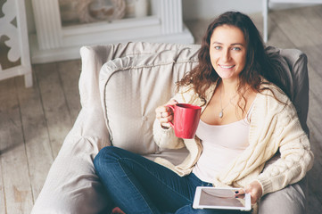 Cozy reading. Relaxing at home. Young woman with cup of tea using tablet computer.