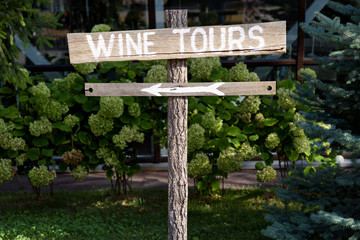 Wooden wine tour sign with arrow with green shrubs on background