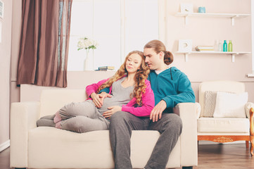Happy pregnant woman with her husband on a sofa in the room