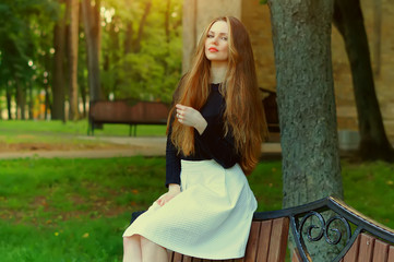 Attractive young sexy woman with red lips and great hair, enjoying her time outside in park with green trees on background.