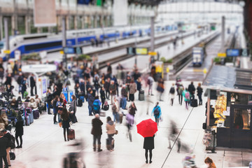 woman with red umbrella waiting at train station and blurred people in motion, solitude concept - Powered by Adobe