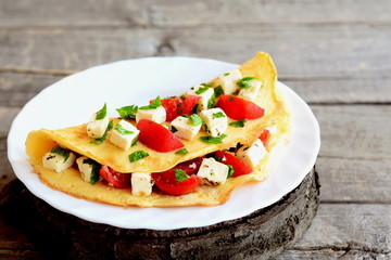 Fried omelet stuffed with cheese, tomatoes and parsley. Stuffed omelette on a plate and on old wooden background. Easy egg omelet recipe. Closeup