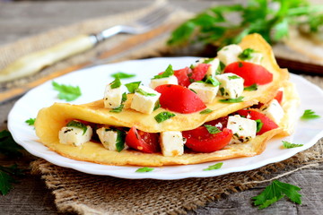Home stuffed omelet on a plate. Egg omelet stuffed with tomatoes, cheese and green parsley. Vegetarian diet breakfast recipe. Fork, knife, cutting board on wooden background. Closeup - obrazy, fototapety, plakaty