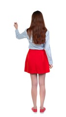 back view of writing beautiful woman. Long-haired brunette in red skirt draws a felt-tip pen on the wall.