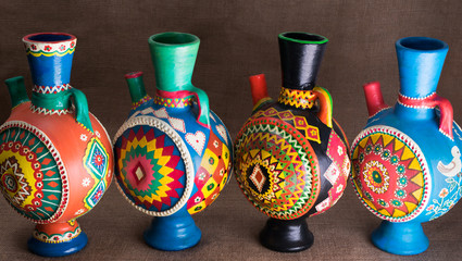 Four decorated colorful handcrafted pottery jugs on sackcloth background