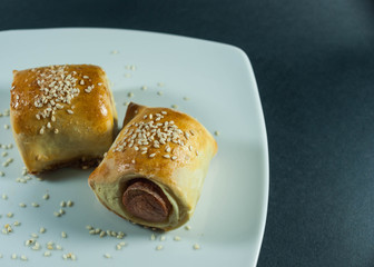 sausage roll in the dough on a white plate on the black backgrou