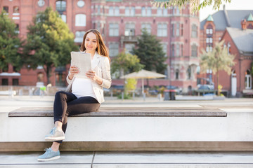 Fototapeta na wymiar Pregnant businesswoman is reading thenewspaper on a bench