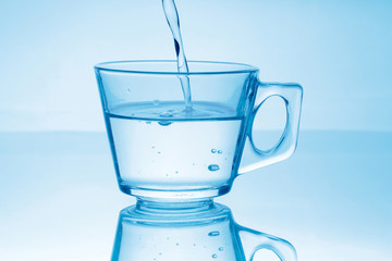 Pouring water into glass on blue background