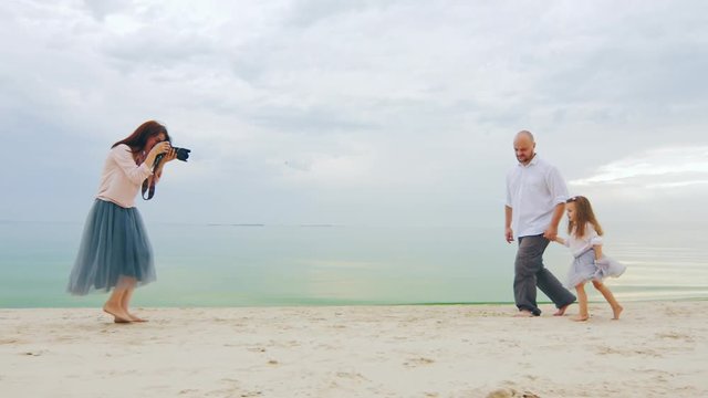 Family photo shoot. Mom takes pictures dad and daughter on the beach