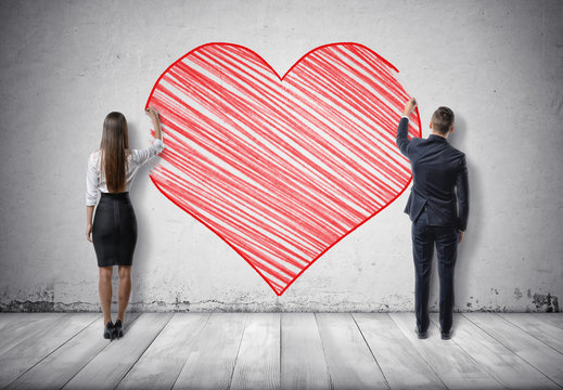 Businessman and businesswoman drawing big red heart on concrete wall