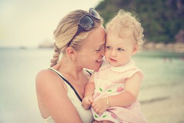 smiling mother hugs her little curly daughter while on vacation at the beach. Mom leaned to face the child. The concept of family happiness