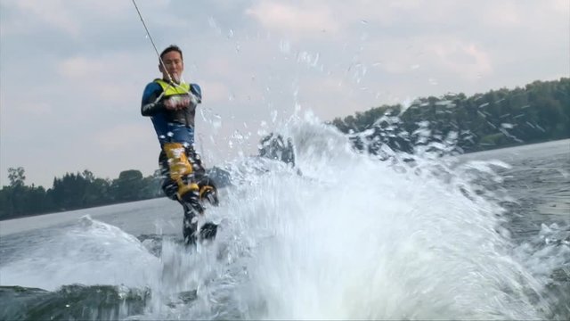 Wakeboarder man in diving suit riding the wave and crush in cold water