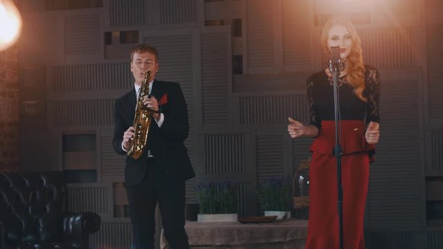 Jazz duet perform on stage. Saxophonist in suit. Singer in retro style. dress. Lights. Click fingers
