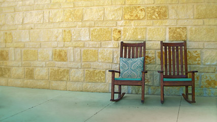 Fototapeta na wymiar A couple of rocking chairs by yellow stone wall