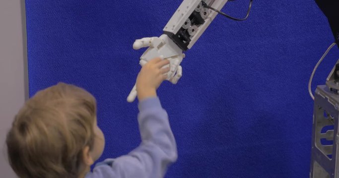 Close up view of small boy hand holds white plastic moving hand of humanoid robot in Robotics exhibition and conference ECC Sokolniki. Moscow, Russia