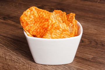 Potato crisps in bowl on wooden board, concept of unhealthy food
