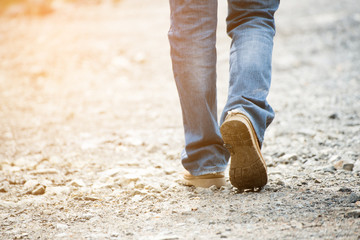 Legs of Lonely man wearing jeans and leather boots walking along the path strewn with rocks. Travel Concept.