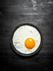 Fried egg in a frying pan. On black wooden background.