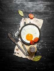 Fried egg with spices. On black wooden background.