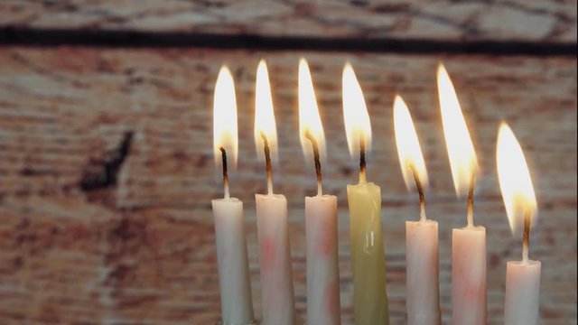 Chanukah candles all in a row. Bright, shiny multicolor candles for the Jewish holiday. All lit, isolated on a black background, horizontal view.
