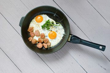 fried eggs with grilled meat on pan. light wood background, view from above