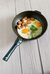 fried eggs with grilled meat on pan. light wood background, view from above