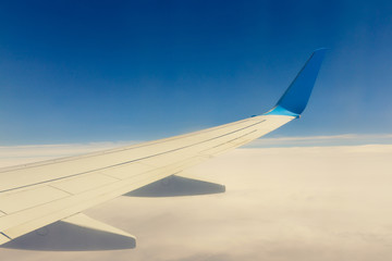 Fototapeta na wymiar Wing of an airplane flying above the clouds on blue sky background