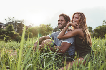 Affectionate young couple sitting on rural grass - obrazy, fototapety, plakaty