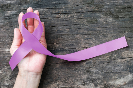 Lavender purple cancer (all kinds) awareness ribbon on human hand, aged wood background: Ribbon color symbolic concept raising public support campaign on people health living with disease