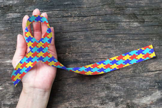 World Autism awareness day WAAD, April 2: Colorful Puzzle fabric ribbon logo color splashed on human hand background raising public support campaign on people's life living w/ mental health illness
