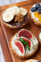 Bagels with different toppings - with cream cheese, figs, bananas, chocolate and blueberries for breakfast on a board, top view