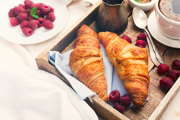 Morning breakfast in bed with cup of coffee, croissants, fresh berries and honey on wooden tray, selective focus