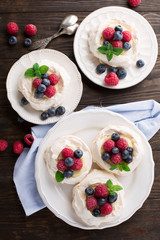 Meringues Pavlova cakes with fresh raspberry and blueberry on dark rustic wooden background, top view