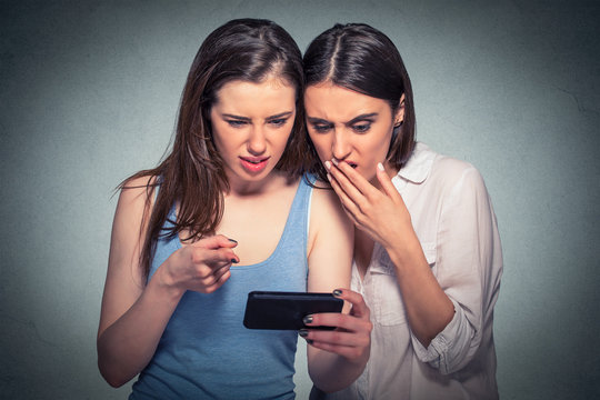 Two displeased women looking at mobile phone