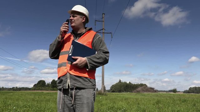 Electrical Engineer talking on walkie-talkie and walk near high-voltage lines