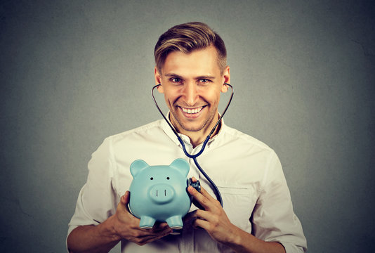 Happy successful man listening to piggy bank with stethoscope