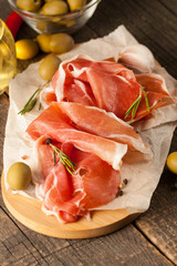 closeup of thin slices of prosciutto, jamon and ham with mixed olives and paprika on wooden cutting board