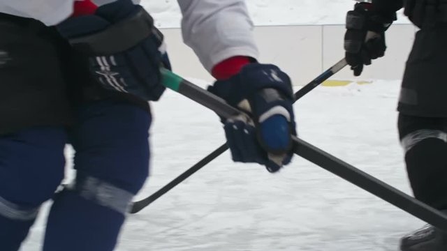Slow motion tracking low section shot of hockey forward player dribbling puck and scoring goal in winter on outside ice rink
