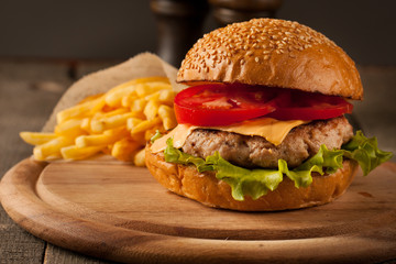 Home made hamburger with beef, onion, tomato, lettuce and cheese. Fresh burger closeup on wooden rustic table with potato fries and chips.
