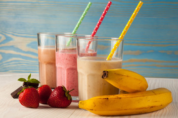 Long glasses of milkshakes with chocolate, strawberry, banana, with ice cream on white and blue background. Shakes and smoothies. Milk shake and cocktail for summer