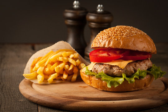 Home made hamburger with beef, onion, tomato, lettuce and cheese. Fresh burger closeup on wooden rustic table with potato fries and chips.